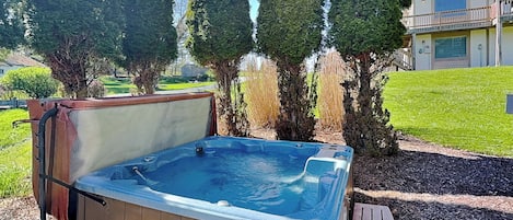 Un bain à remous avec une structure extérieure en bois, entouré d’une pelouse et de grands arbres.