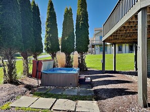A hot tub in a backyard with a wooden deck and tall trees. - Ski Boots N' Bathing Suits by Taylor Made Deep Creek (McHenry)