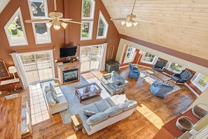 A spacious living room with a fireplace, multiple seating areas, and large windows offering views of the outdoors. - Ski Boots N' Bathing Suits by Taylor Made Deep Creek (McHenry)