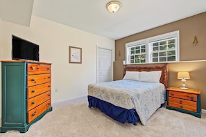 A bedroom with a bed, dresser, nightstand, and a television.