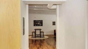 Un pasillo con una puerta de madera, una mesa redonda con sillas, y dos cuadros en la pared.