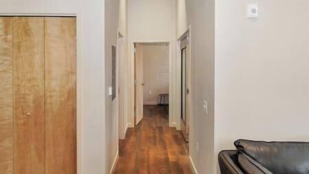 Un couloir étroit avec un plancher en bois, des murs blancs et une porte sur le côté gauche.