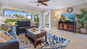 A spacious living room with a ceiling fan, a large TV, and a view of the ocean through large windows. - Sweet EmOCEAN at Jupiter Bay. (Jupiter)