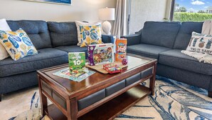 A living room with two grey sofas, a wooden coffee table with children's games, and a view of the outdoors. - Sweet EmOCEAN at Jupiter Bay. (Jupiter)