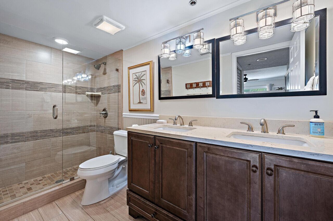 Un baño moderno con ducha de vidrio, tocador doble y un espejo grande.