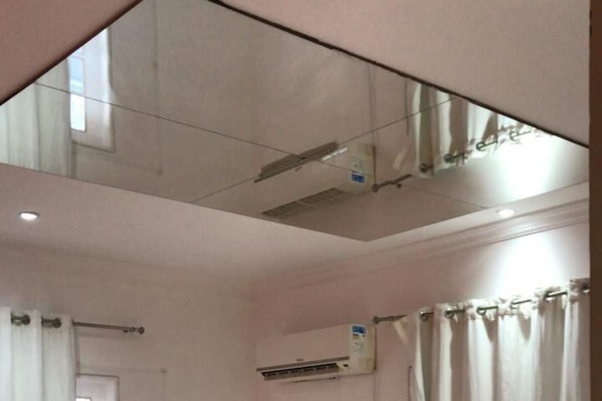A hotel room with a bed, a bedside table, a mirror, and an air conditioning unit.