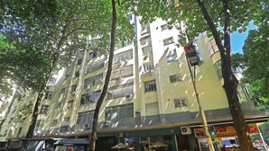 Um edifício com vários andares, varandas, um café no nível da rua e carros estacionados.