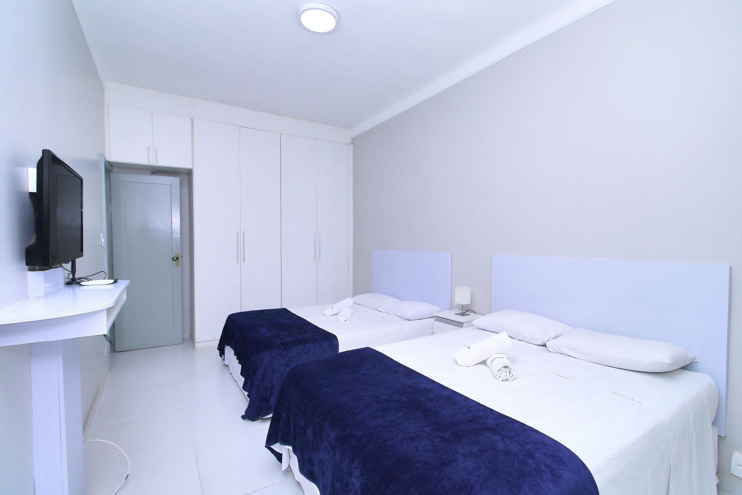 A hotel room with two beds, a TV on a stand, and a door leading to a closet.