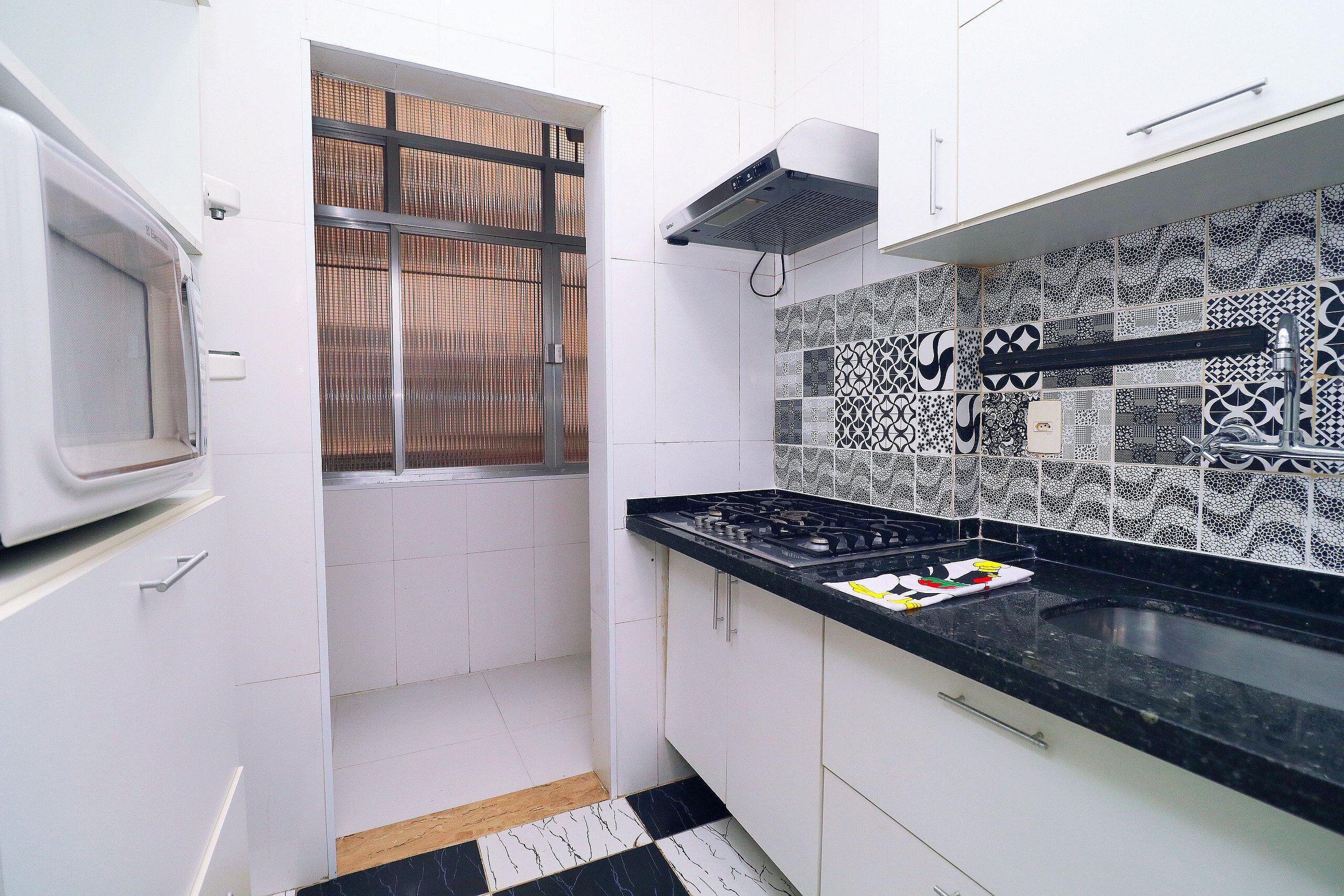 A kitchen with white cabinets, a black countertop, a stove, and patterned backsplash tiles.