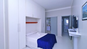 Een slaapkamer met een bed, een bureau met een computer, een televisie en een kledingkast.