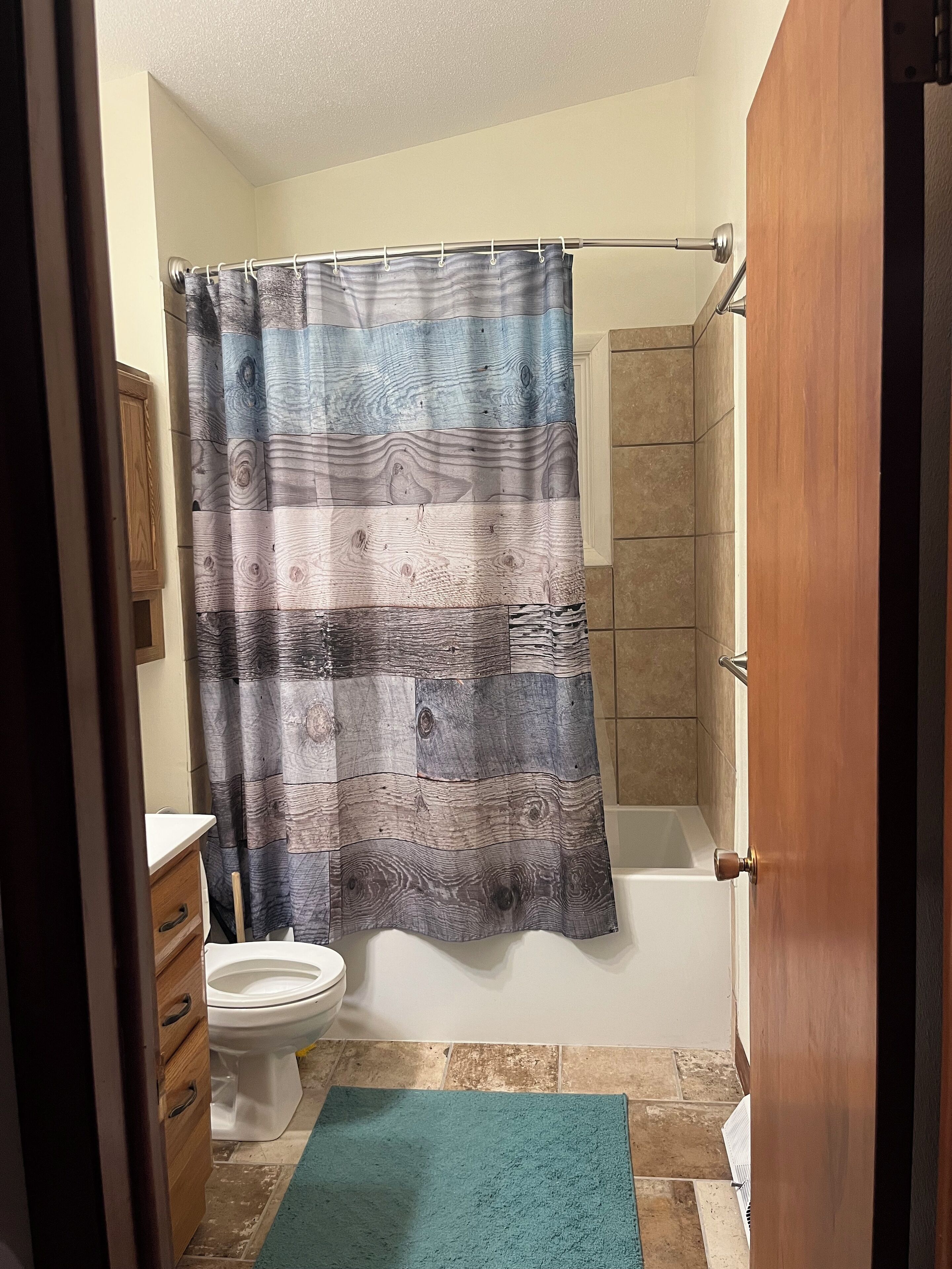 Ein Badezimmer mit Duschvorhang, Toilette, Waschbecken und einem Holzkabinent.