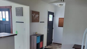 A hallway with a tiled floor, a ceiling fan, a small table, and a door with a window. - Kadia’s Place-The One With The Pool Table & TVs (Cedar Rapids)