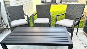 A patio with a black metal table and three wicker chairs with cushions. - Kadia’s Place-The One With The Pool Table & TVs (Cedar Rapids)