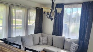 A cozy living room with a wooden dining table, a beige sectional sofa, and a chandelier. - Kadia’s Place-The One With The Pool Table & TVs (Cedar Rapids)