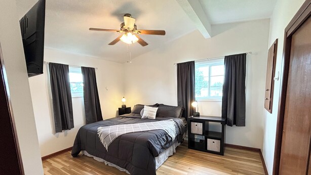 A bedroom with a bed, a nightstand, a ceiling fan, and a window with curtains. - Kadia’s Place-The One With The Pool Table & TVs (Cedar Rapids)