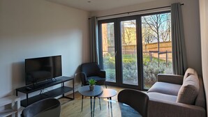 Una sala de estar moderna con un televisor de pantalla plana, un sofá, una silla y una mesita con una planta.