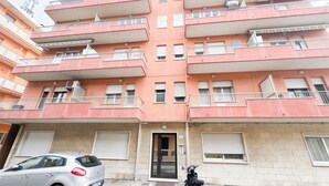 A multi-story residential building with balconies, a car parked in front, and a motorcycle beside the entrance. - Esperia Apartment by Ca-Sa Check (Chioggia)