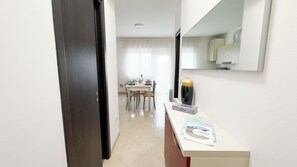 Un pasillo de hotel con un área de comedor al fondo, un mostrador de recepción blanco y un espejo grande en la pared.