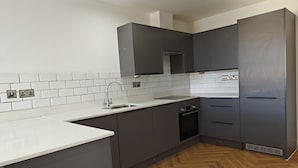 A modern kitchen with grey cabinets, a white countertop, and a herringbone wood floor. - 2-bed Apartment Birmingham Snow Hill (Birmingham)