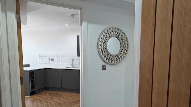 A modern kitchen with grey cabinets, a white countertop, and a circular decorative mirror on the wall. - 2-bed Apartment Birmingham Snow Hill (Birmingham)