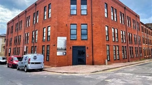 A red brick building with a corner entrance and multiple windows. - 2-bed Apartment Birmingham Snow Hill (Birmingham)