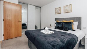 A modern bedroom with a large bed, a wooden door, and two wall-mounted artworks. - 2-bed Apartment Birmingham Snow Hill (Birmingham)