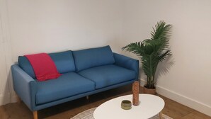 En blå sofa med et rødt tæppe, en lille potteplante og et rundt bord med et mønstret gulvtæppe.