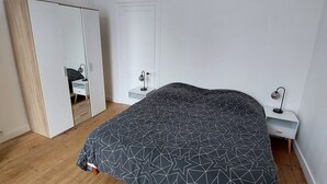 Et soveværelse med seng, garderobe, natbord og sengebord.