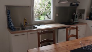 Et kompakt køkken med et vindue, en vask, en kaffemaskine og et spiseområde med et træbord og stole.