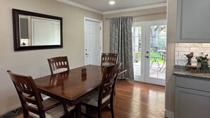 Un comedor con una mesa y sillas de madera, un espejo en la pared y vistas al exterior a través de un ventanal.