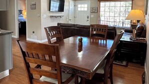 Un comedor con una mesa y sillas de madera, un televisor sobre la mesa y una ventana con persianas.