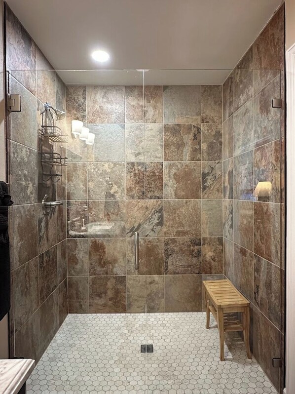 A shower with a wooden bench, a towel rack, and a hand dryer.