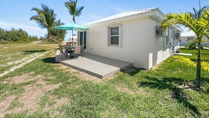 A small, single-story house with a patio, a table and chairs, and a blue umbrella. - Golf Cart Included, Andros Villa, Treasure Cay, Bahamas, 100 yards from beach (Treasure Cay)
