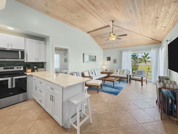 A spacious living area with a kitchen, a ceiling fan, and a view of palm trees. - Golf Cart Included, Andros Villa, Treasure Cay, Bahamas, 100 yards from beach (Treasure Cay)