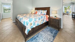 A bedroom with a wooden ceiling, a bed with a floral bedspread, a nightstand with a lamp, and a view of the outside through a door. - Golf Cart Included, Andros Villa, Treasure Cay, Bahamas, 100 yards from beach (Treasure Cay)