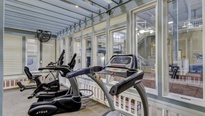 Een fitnessruimte met trainingsapparatuur, grote ramen en uitzicht op een balkon.