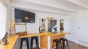 A modern kitchen with a wooden island, black bar stools, a flat-screen TV, and a staircase leading to a loft area. - Panferio Paradise, Water Front Home (Pensacola Beach)