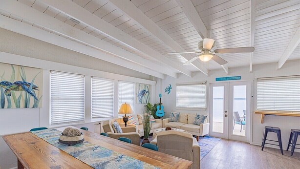 A spacious living area with a wooden dining table, multiple seating options, a ceiling fan, and a view through the glass doors. - Panferio Paradise, Water Front Home (Pensacola Beach)