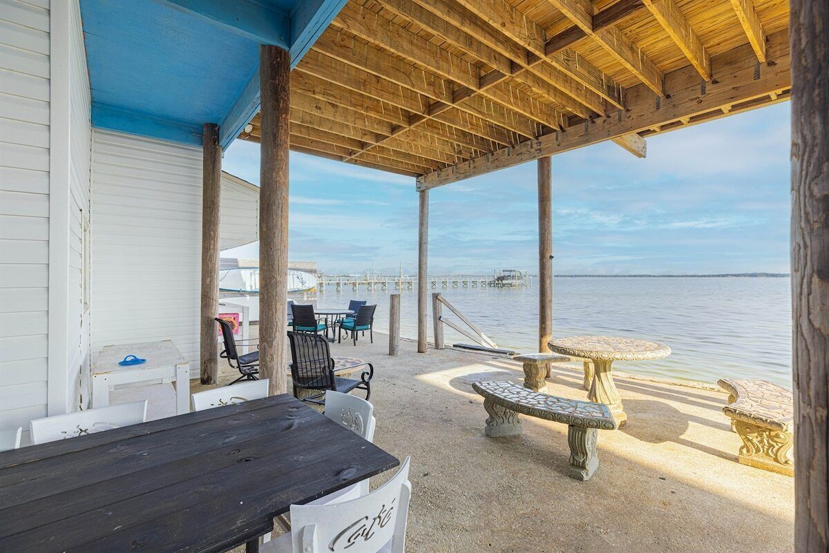 A covered outdoor seating area with tables and chairs, a stone bench, and a view of the water.
