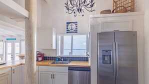 A modern kitchen with white cabinets, a stainless steel refrigerator, a built-in dishwasher, a window with a view, and a chandelier. - Panferio Paradise, Water Front Home (Pensacola Beach)