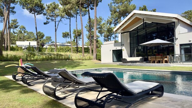 A modern house with a swimming pool, surrounded by tall trees and equipped with outdoor furniture. - Quiet Villa with wonderful views of the golf courses! (Almada)