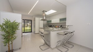 A modern kitchen with a central island, stainless steel bar stools, and a large window overlooking a garden. - Quiet Villa with wonderful views of the golf courses! (Almada)