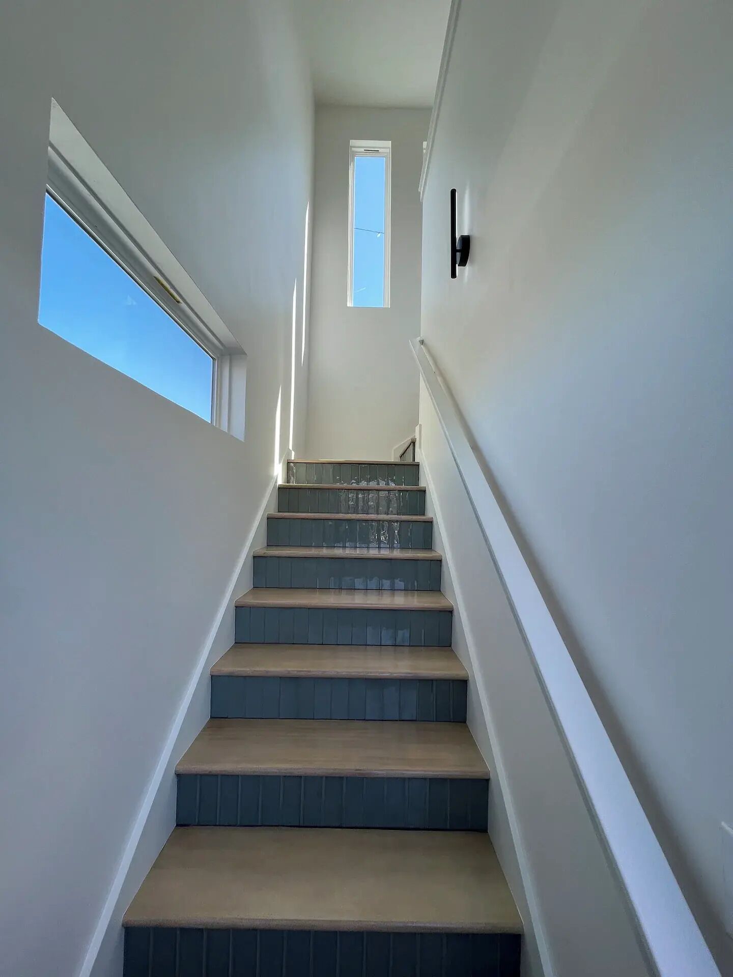 Eine Treppe mit Geländer auf der rechten Seite, die zu einer Zwischenebene mit Tür und Fenster führt.