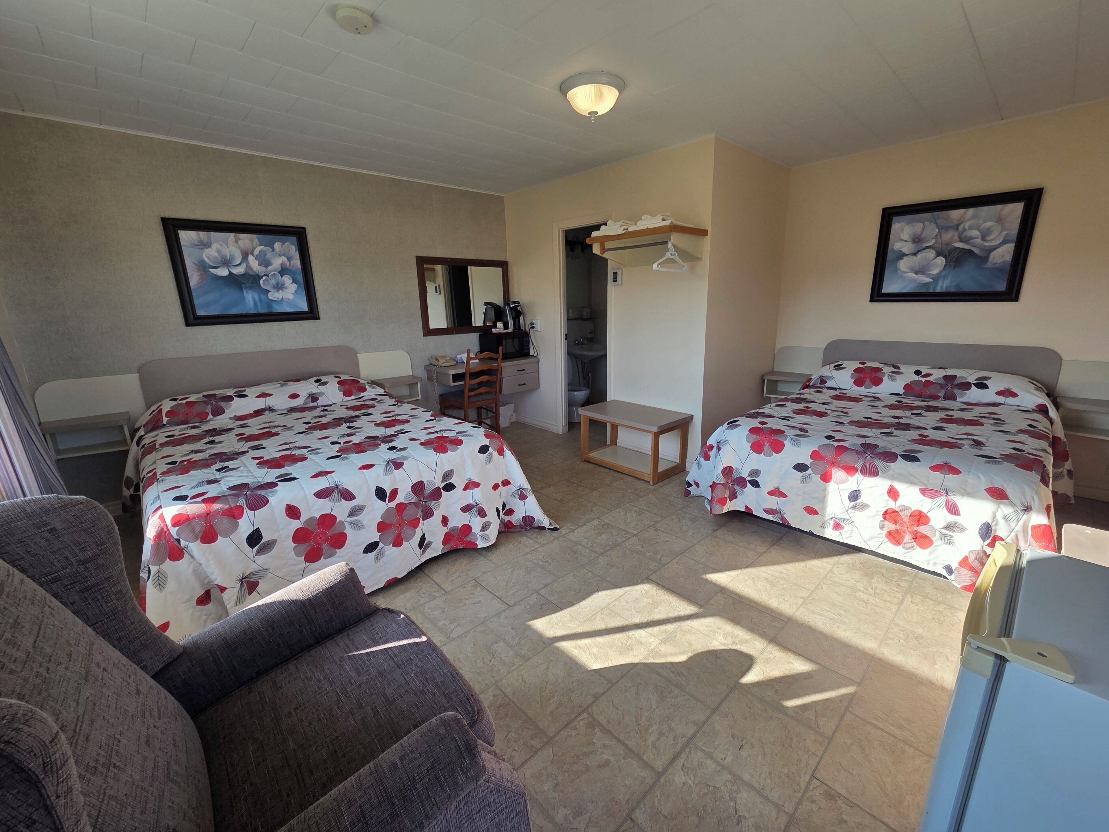 A hotel room with two beds, a desk, a chair, a small table, and a bathroom visible through an open door.