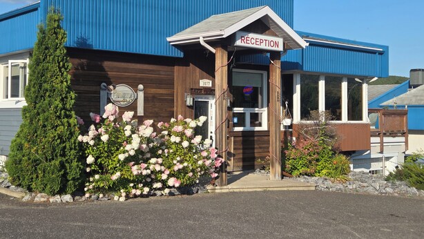 A building with a reception area, wooden exterior, and a blue roof. - Motel Claude (Degelis)