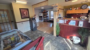 A hotel lobby with an ATM, a reception desk, a clock, and a vending machine. - Motel Claude (Degelis)