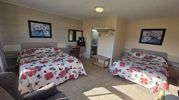 A hotel room with two beds, a desk, a chair, a small table, a mirror, and a bathroom visible through an open door.