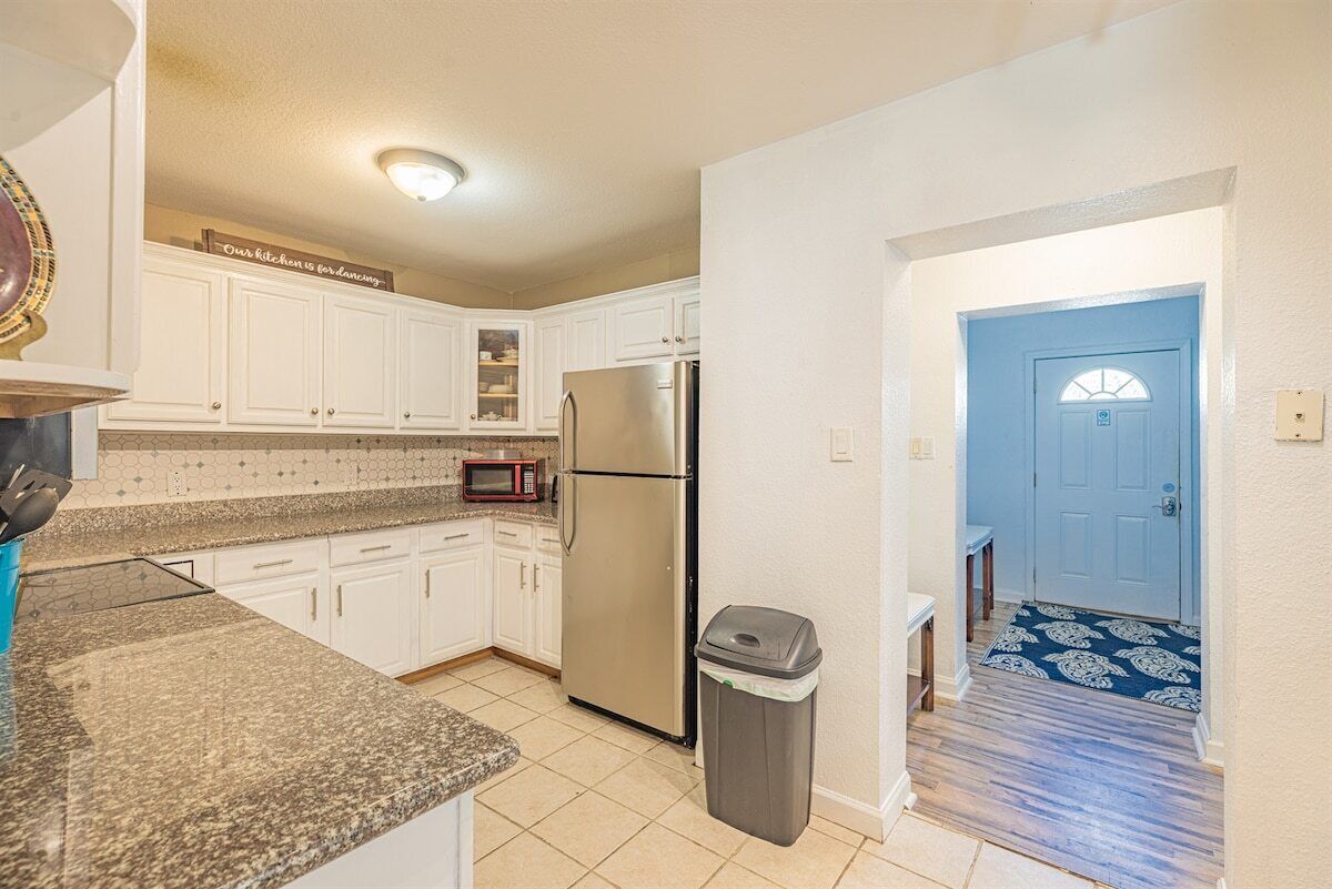 A kitchen with white cabinets, a stainless steel refrigerator, a microwave, and a trash can.