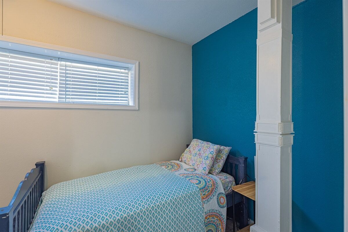 Une chambre à coucher avec un lit, une fenêtre avec des stores, un mur bleu et une colonne blanche.