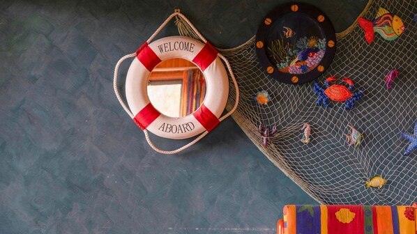 A lifebuoy with "WELCOME" and "BOARD" text, a net with colorful fish and sea creatures, and a dark textured background. - Step Back in Time - Safety Beach (Safety Beach)